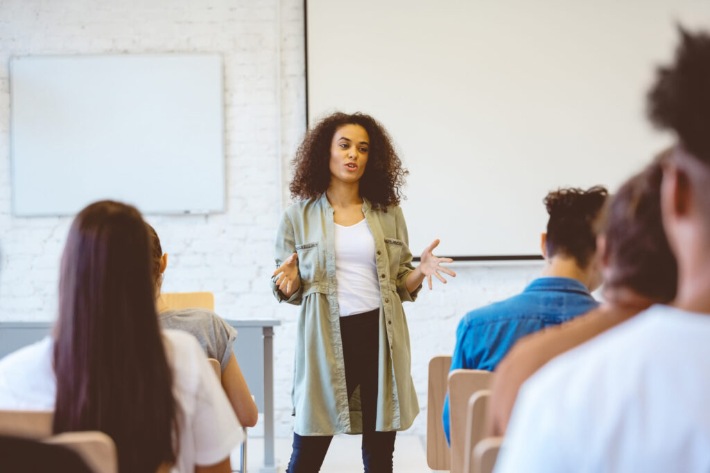 Female student gesturing while explaining during presentation. Young woman is giving speech in classroom. She is sharing ideas with classmates.